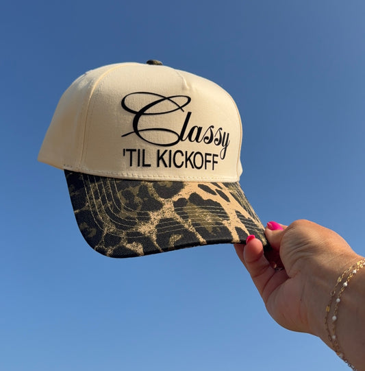 Beige cap with 'Classy 'Til Kickoff' text held against a clear blue sky